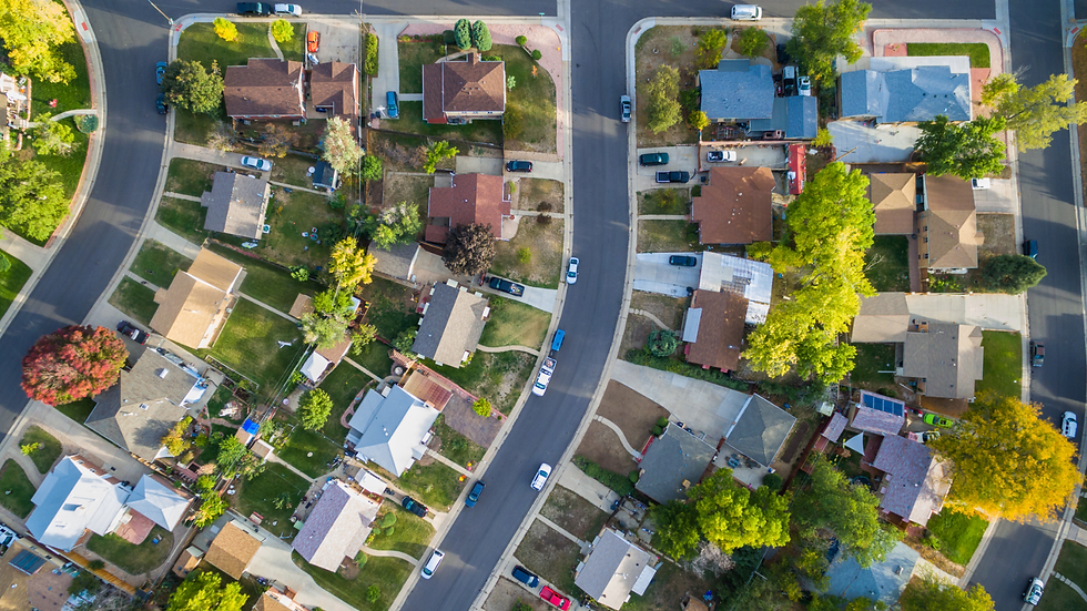 Aerial drone view of a suburban residential neighborhood featuring curved streets lined with single-family homes, driveways, parked cars, green lawns, and mature trees.