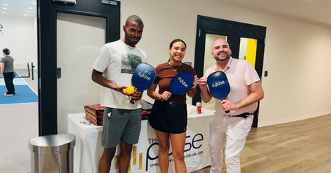 Three residents of The Pulse OKC smiling and holding pickleball paddles that say The Pulse on them.