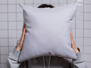 A woman holding a pillow in front of her face representing pillow face from too much filler.