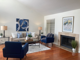 An open floor plan room that has been staged, showing blue chairs and a fireplace.