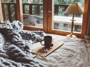 A cozy bed with a knit blanket in front of a glass door that leads to a deck.