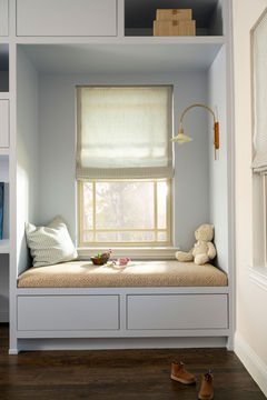Cushioned window seat built into pale blue cabinetry with drawers, shelving and a teddy bear.