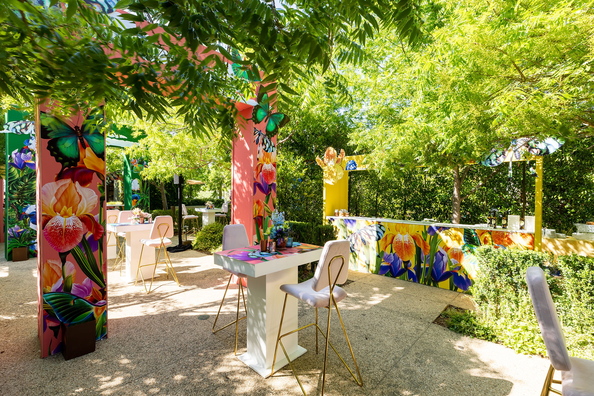 Outdoor seating with bright printed high-top tables and greenery backdrop.