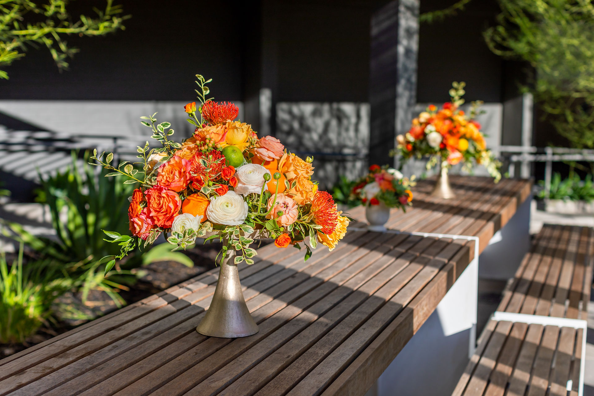 Orange and white floral arrangements on wooden counters at a corporate summer event.