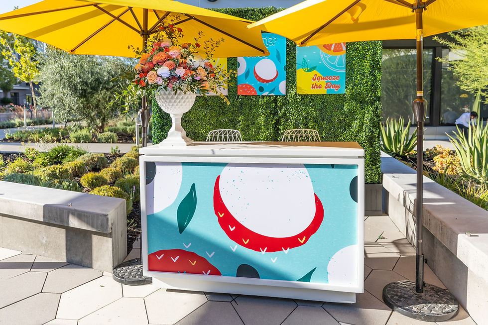 Citrus-themed beverage bar with floral arrangement and yellow umbrellas at a corporate summer reception.