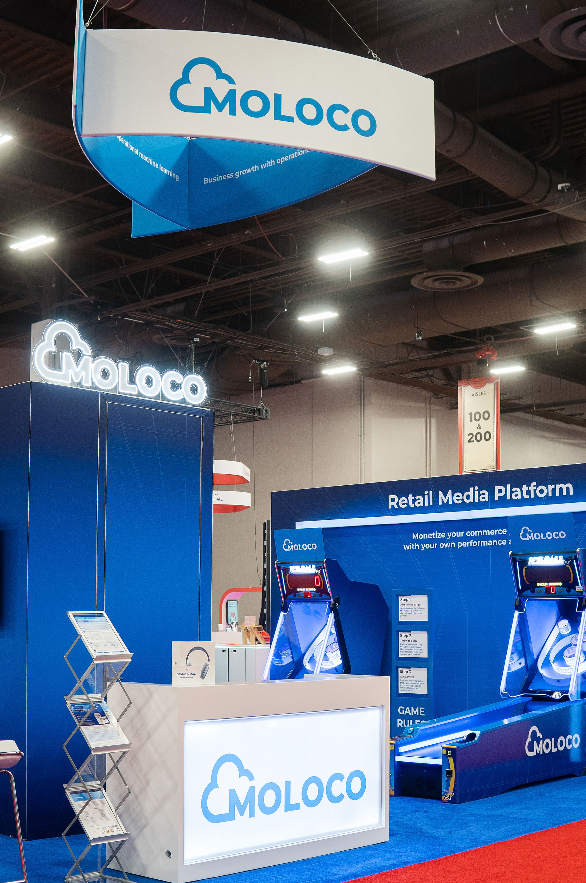 Branded exhibit booth for MOLOCO with overhead signage and arcade game integration