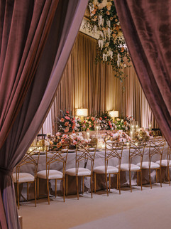 Luxury wedding dinner with velvet draping, floral ceiling decor, and gold chairs