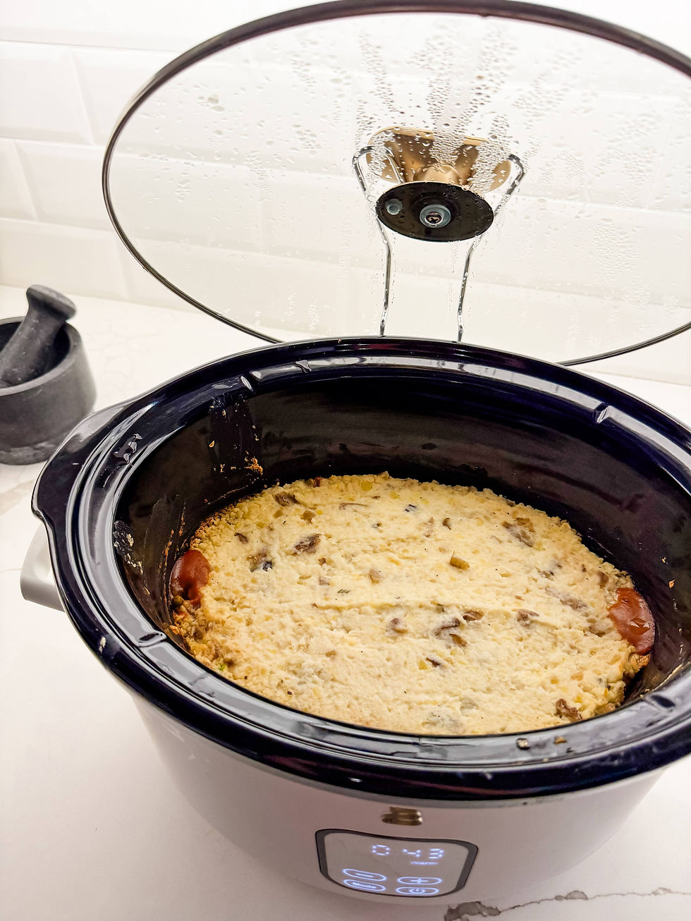 Slow cooker with a glass lid slightly open, showing a cooked Shepherd's Pie inside. Mortar and pestle in the background.