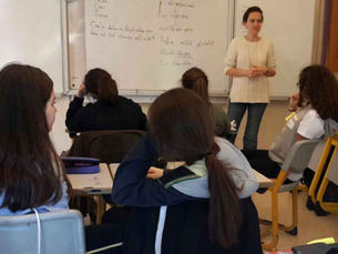 Sınıfta öğretmen beyaz tahtada yazarken öğrenciler sıralarda dinliyor; arka planda el yazısı notlar. Özge Özdemir P4C uygulaması yaparken.