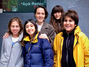 Açık Radyo önünde dört çocuk ve bir kadın gülümseyerek poz veriyor; sarı ve mavi montlar dikkat çekiyor. Küçük Düşünürler Topluluğu.