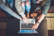 Three women lean over a laptop on a coffee table, pointing at the keyboard and screen, in a casual indoor meeting on Bookdio.