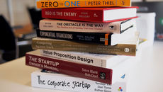Stack of startup and business books on a desk, including Zero to One and The Corporate Startup, with colorful spines.