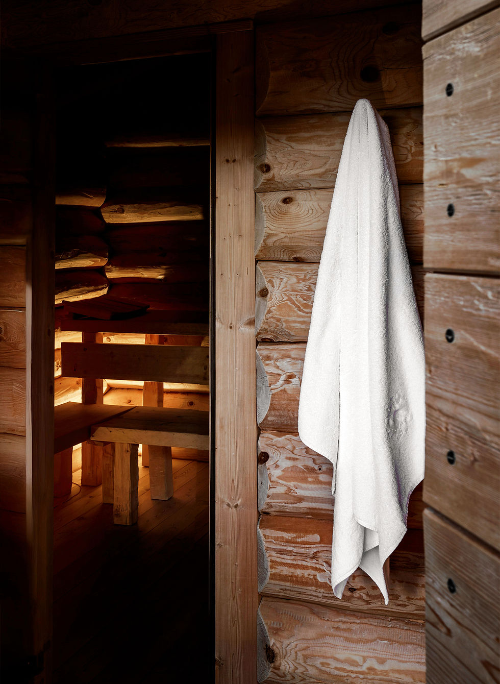 An interior photography close-up focusing on a white cotton towel hanging on an outdoor rustic log wall, offering an outside-in view toward the warm-lit indoor wooden sauna at Tyrol Hotel in Selva di Val Gardena, photo direction and production Laura Pozzi Studio.