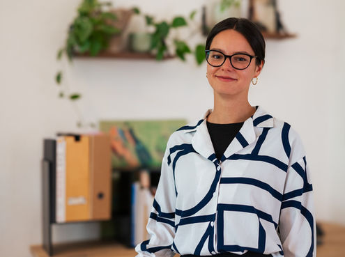 Ein Foto von Katharina Hiller vor einem Schreibtisch, der verschwommen zu sehen ist.