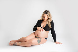 a mummy to be sitting down on the floor, cradling her bump with her hands for her maternity photoshoot in aldershot, hampshire