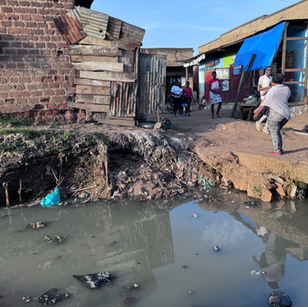 People walking on a muddy road with houses and shops in the background.