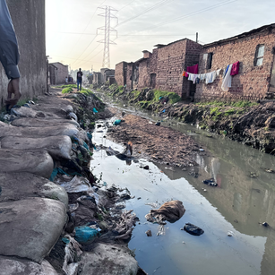 Man walks past trash-filled waterway near Kampala Research Laboratory, Uganda.