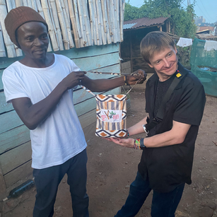 Two men exchanging items, smiling, in front of a building. Speakers for Africa.