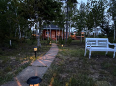 Stone path lit by lanterns leading to a red cottage, screened in room, and hot tub at dusk.