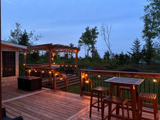 Wooden deck with string lights, outdoor bar furniture, and hot tub at dusk