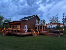 Wooden cabin with string lights on the deck, screen in room, and hot tub.