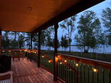 Wooden deck with string lights overlooking trees and ocean at dusk.