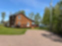 Brown wooden cottage with a large deck and gravel driveway on ocean.