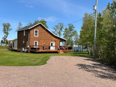 Wooden cottage with a large deck and gravel driveway with ocean view.