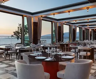 Set dining tables at Pagos Rooftop with panoramic views of İzmir Bay at sunset.