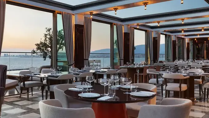 Set dining tables at Pagos Rooftop with panoramic views of İzmir Bay at sunset.