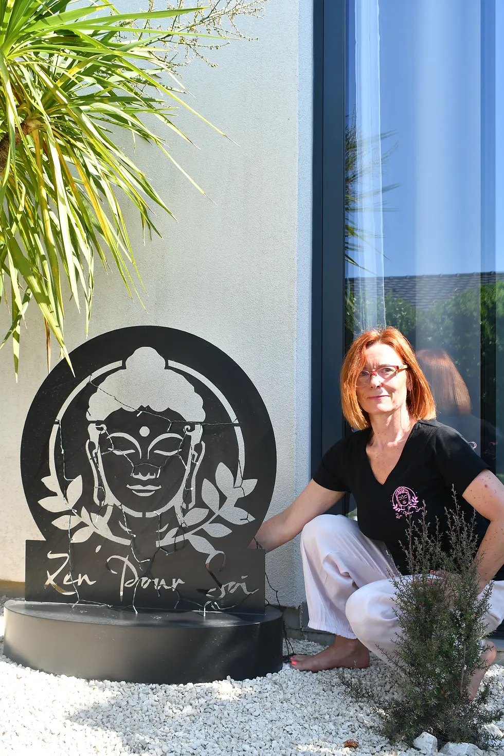 Femme  pose à côté d'une sculpture de Bouddha dans un jardin ensoleillé. Texte: "Zen pour soi". Plante verte en arrière-plan.