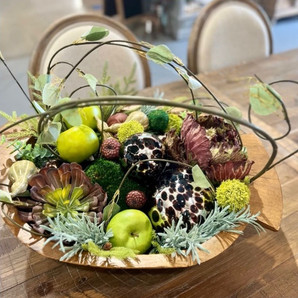 Decorative bowl with faux pears, greenery stems, pods, brown leaves and a silver and brown sphere.