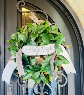 Green wreath with cream ribbon and text reading "O Holy Night". Inspirations Raleigh