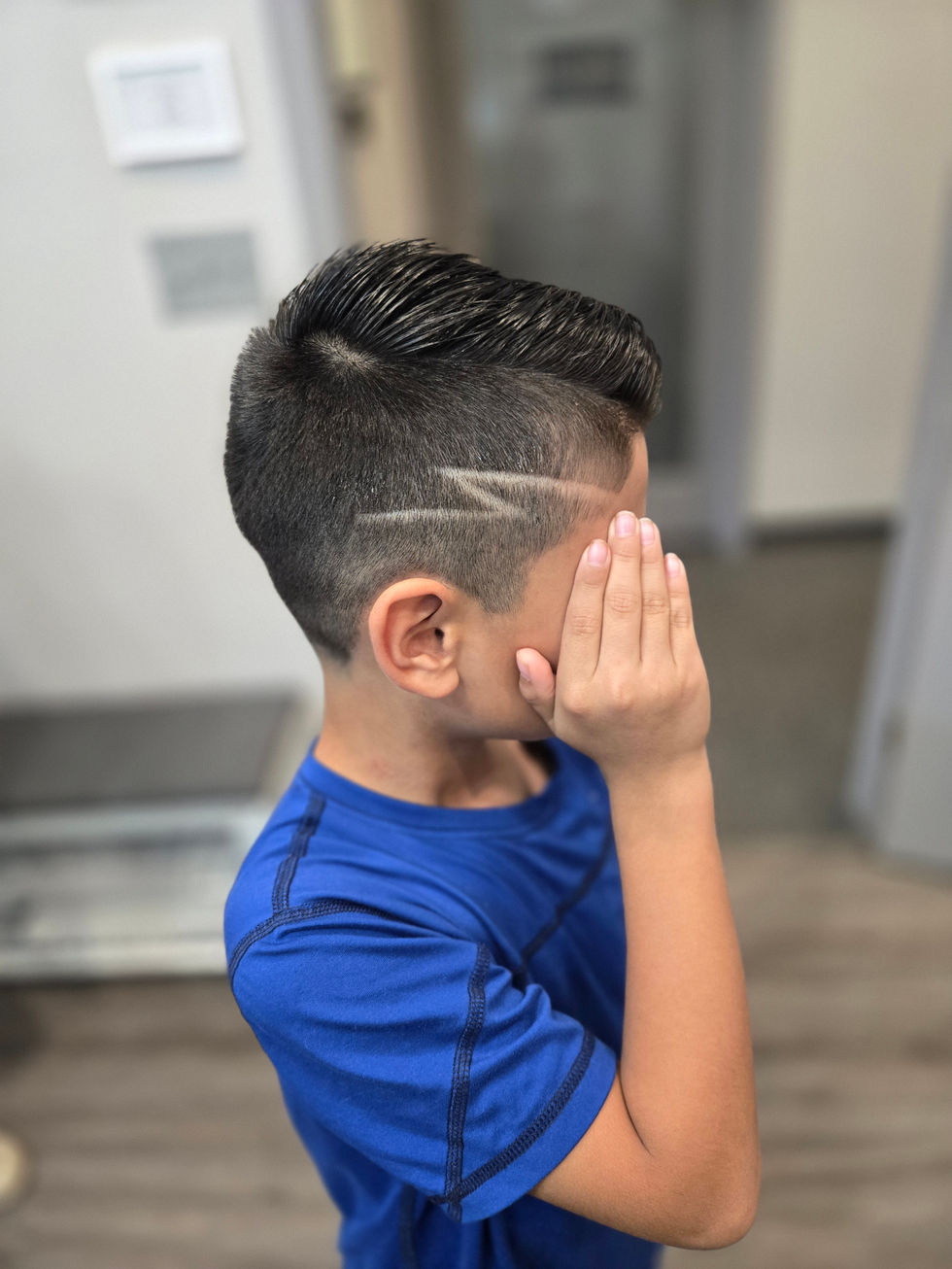 Child with short haircut, hand covering face.