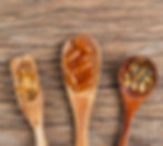 Golden and amber gel capsules fill three wooden spoons, set against a rustic wood backdrop, showcasing KJ Vitality's premium supplements