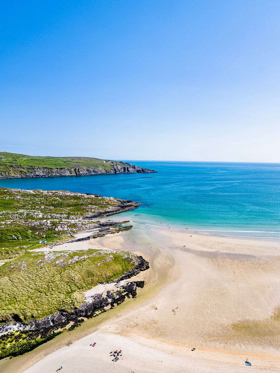 Panoramic view of Barley Cove with shimmering water reflecting the rugged cliffs under a clear sky