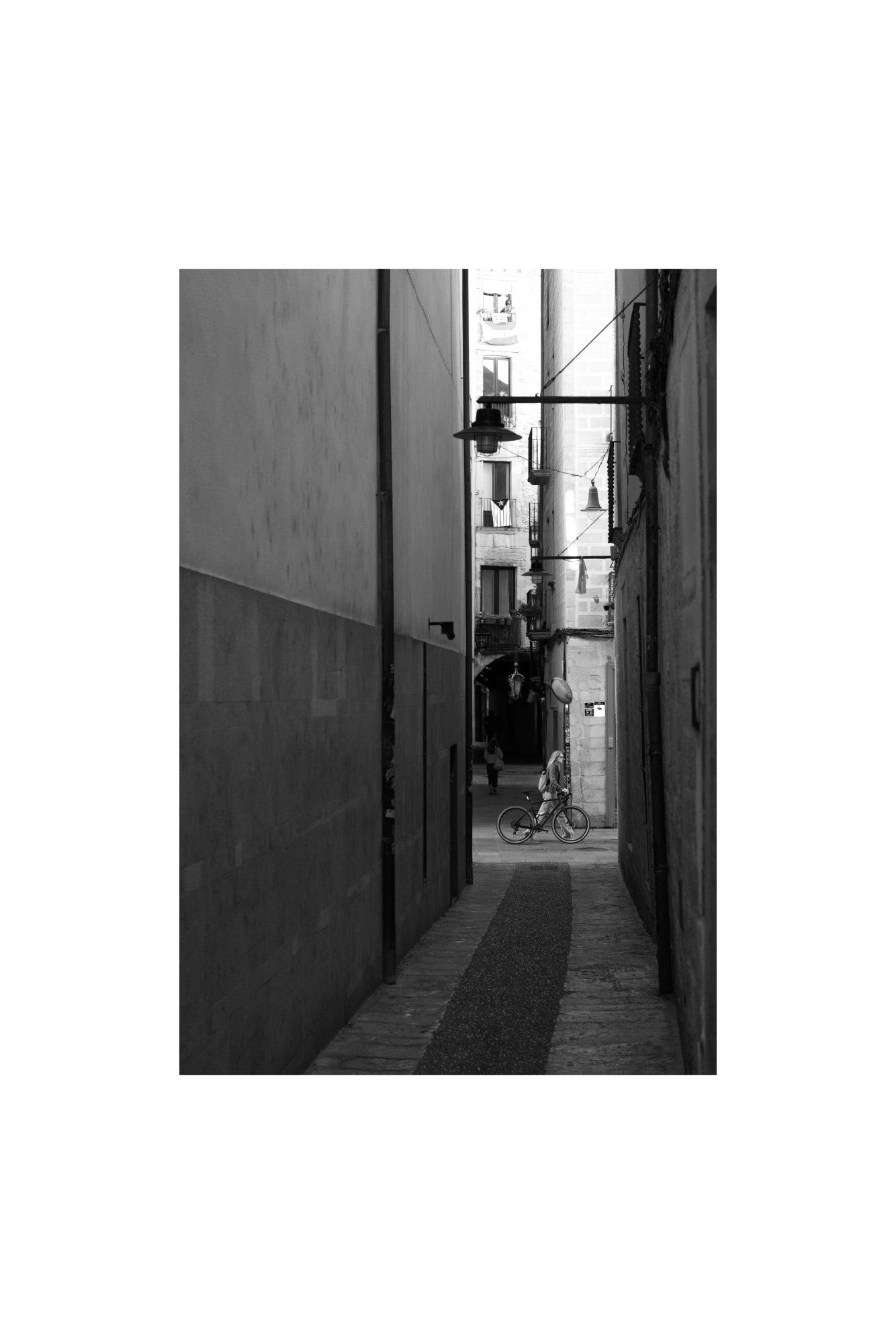 Fotografía en blanco y negro de arquitectura urbana en Girona, una callejuela estrecha y una bicicleta.