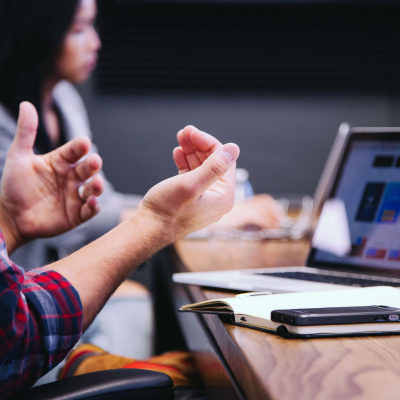 A photo of a person gesturing in front of a laptop in an office context