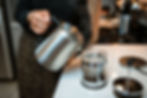 Pouring tea from a stainless steel kettle into a mug, then adding the tea