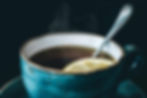 A mug of lemon and honey tea with a spoon and slice of lemon