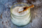 Jar of coconut oil with a small wooden spoon on rustic wooden surface. White, creamy texture contrasts with weathered blue backdrop.