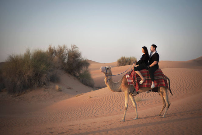 Couple riding a camel across the desert dunes