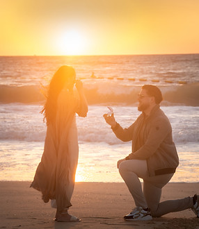 Surprise proposal on the beach at sunset: he kneels with the ring, she covers her face