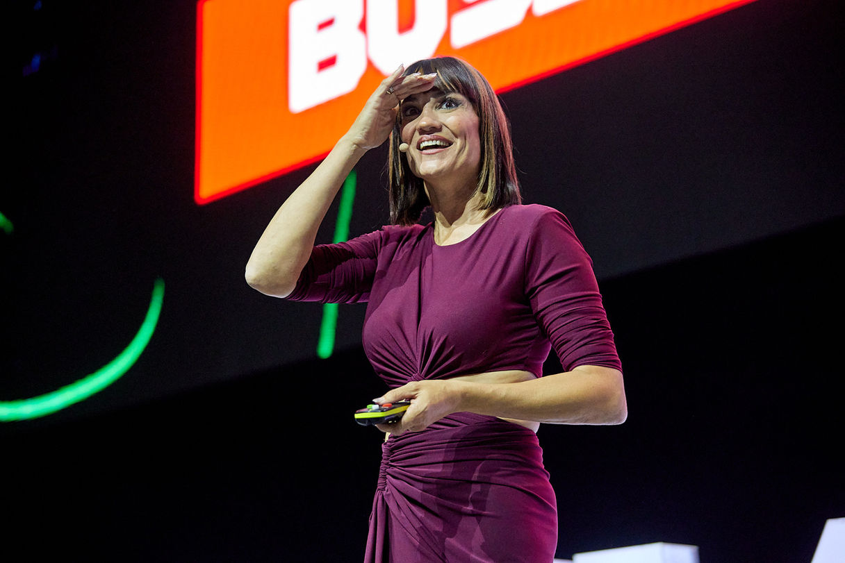 Mujer en escenario de conferencia, mirando hacia arriba y cubriéndose los ojos