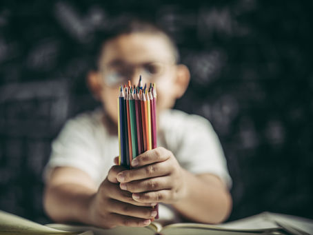 Criança com óculos segurando lápis de cor em ambiente escolar, representando aprendizagem, infância e cultura escolar.