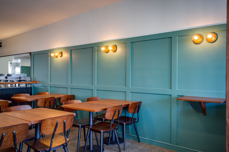 The interior of a restaurant with timber seating, green walls and industrial style lighting.