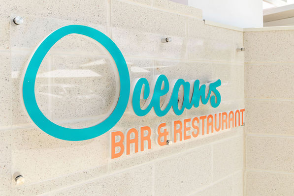 Blue and orange signage reading 'Oceans Bar & Restaurant' on a cream terrazzo brick wall