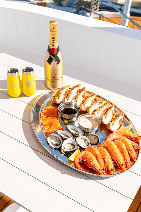 A seafood Platter featuring Prawns, Bugs, oysters and salmon sashimi with wine a two cups next to it