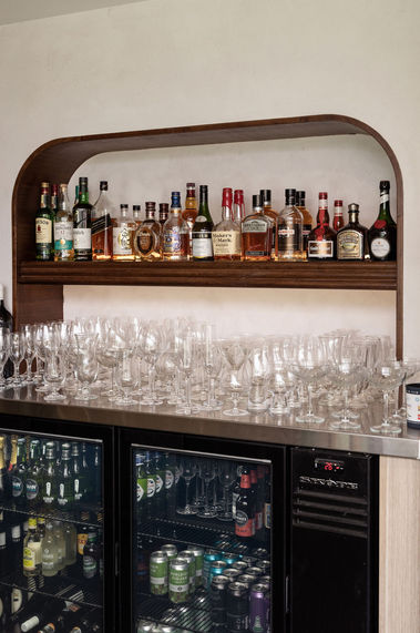 A timber shelf displaying alcohol above a stainless steel counter with wine glasses