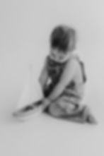 little boy in overalls playing with a wooden boat in simple white studio